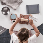 A child plays with a Kids Concept Toy Baking Set, featuring a rolling pin, cookie cutters, a scale, a bowl, and a whisk, encouraging imaginative play and a love for baking. 