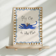 Framed artwork with a blue tiger and text 'fly me to the moon' on a white background