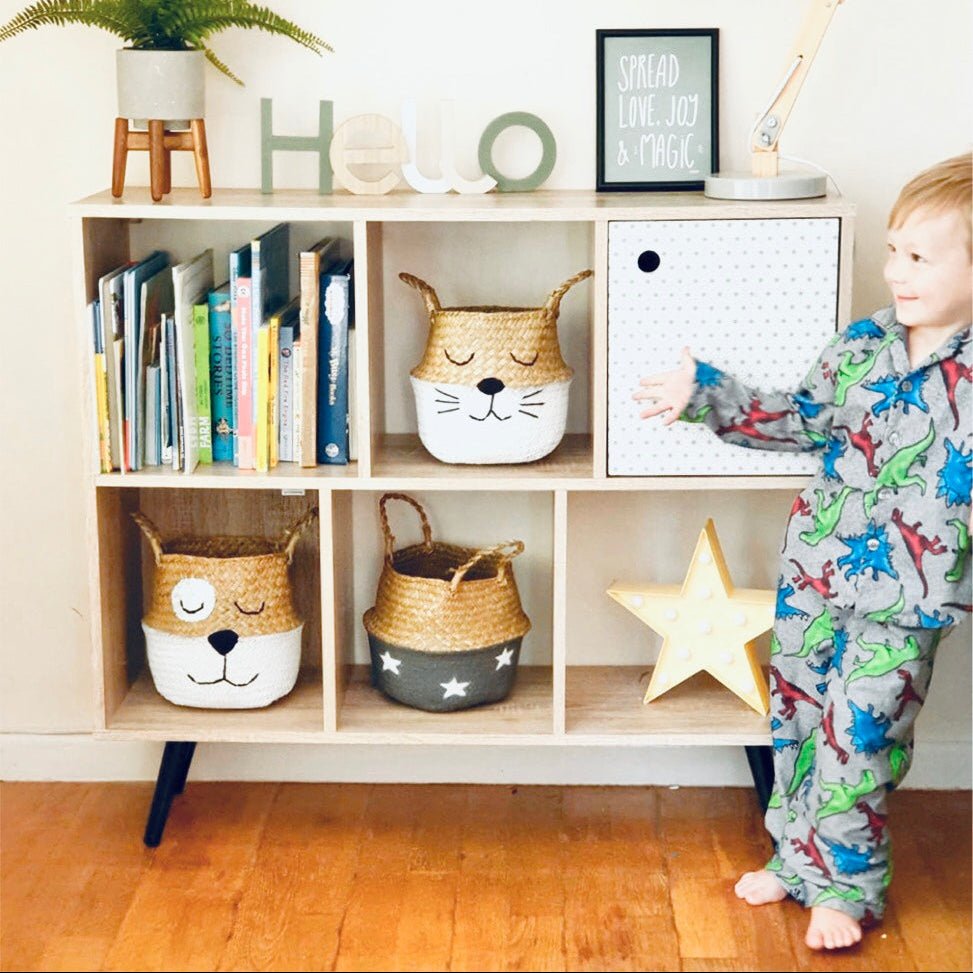 Child in pajamas standing next to a wooden shelf with decorative items and storage baskets.