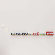 Le Toy Van London Car Set 7 Piece including iconic London wooden vehicles - a double decker bus, a black taxi, a fire engine, a police van, an ambulance, and two sporty cars - arranged in a line on a white surface. 