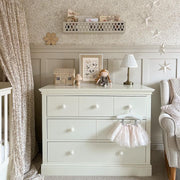 Nursery room with a white dresser, crib, and decorative wall elements.