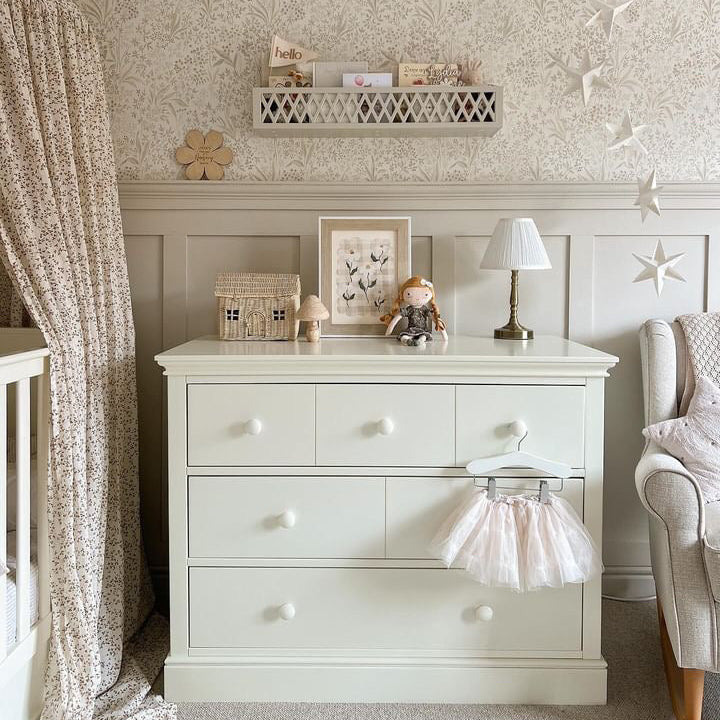 Nursery room with a white dresser, crib, and decorative wall elements.