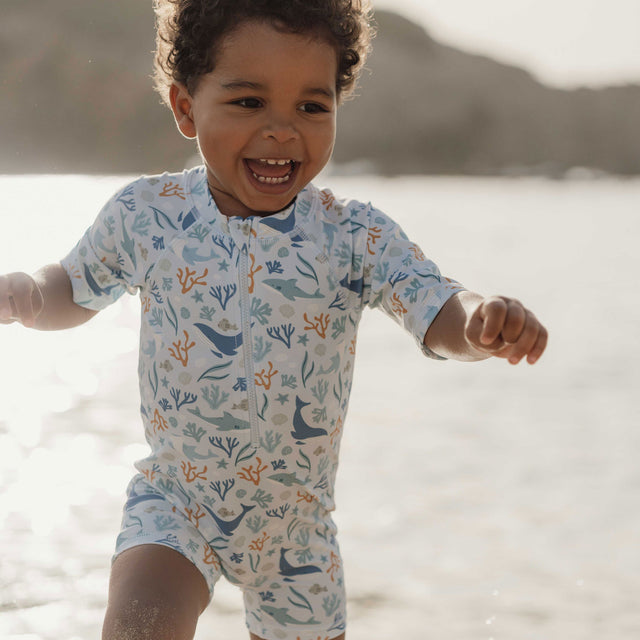 Little Boy Wearing The Little Dutch Short Sleeved Swimsuit In Ocean Dreams Blue