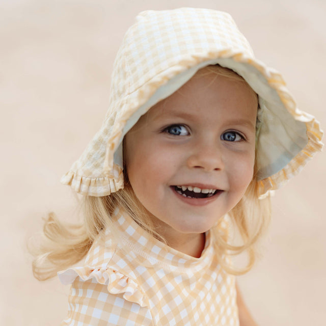 Little girl wearing Little Dutch Reversible Sun Hat In Sea Green & Sunshine Checks
