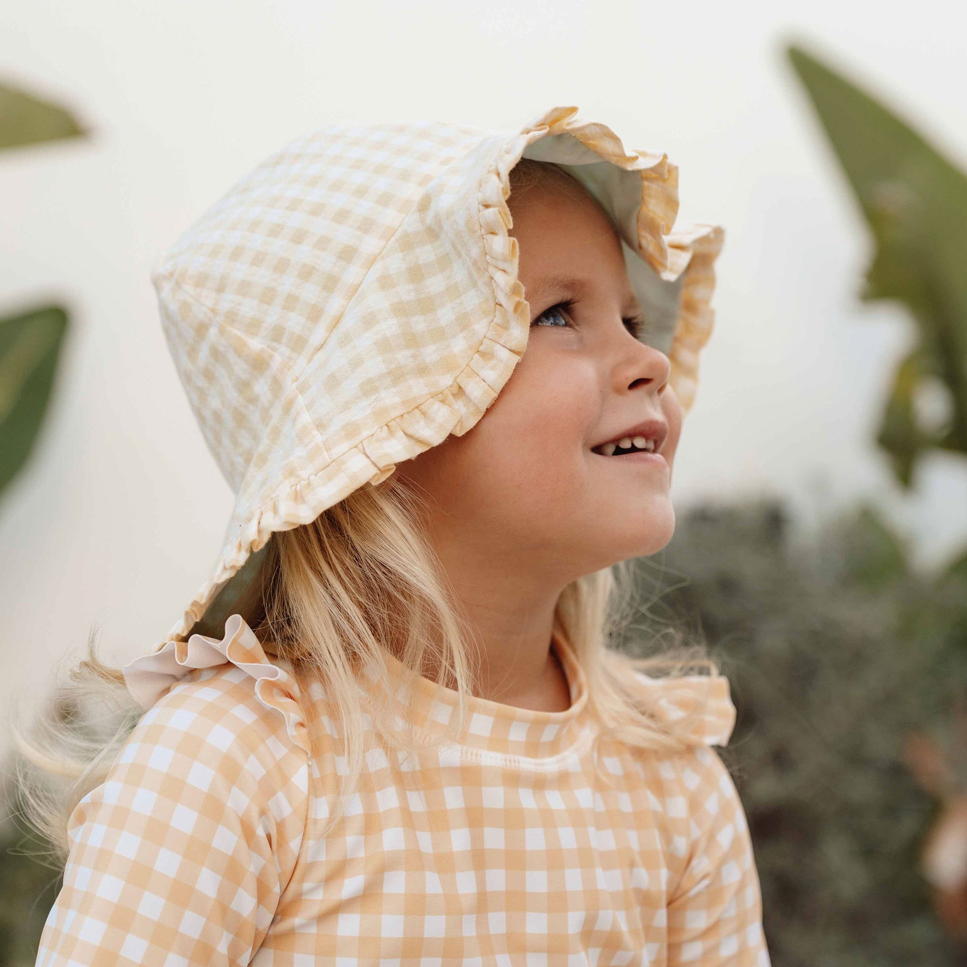 Lifestyle shot of a little girl wearing Little Dutch Reversible Sun Hat In Sea Green & Sunshine Check