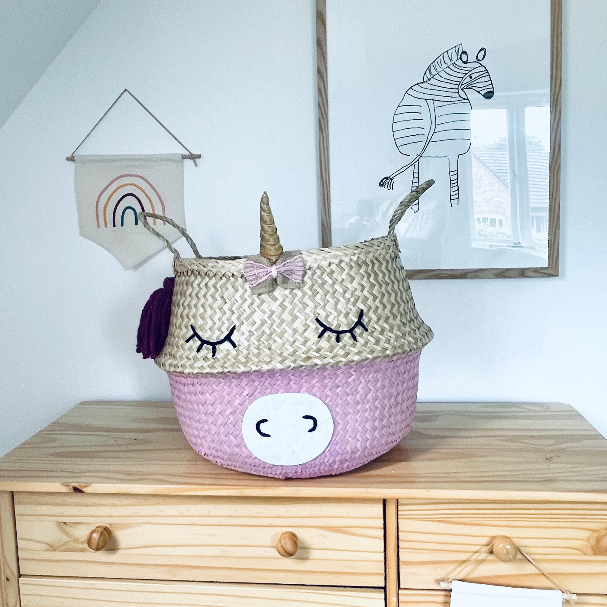 Unicorn-shaped storage basket on a wooden dresser with wall art in the background
