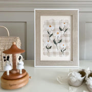 Framed artwork of white flowers on a decorative shelf with a wooden music box and ceramic items.