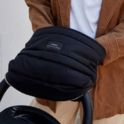 A close-up of a person wearing a Finnson black quilted puffer mono mitten pushing a black pushchair stroller. 