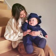Woman holding a baby in a Finnson navy blue snowsuit on a staircase.