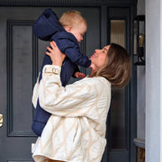 Woman holding a child wearing the Finnson Snowsuit in front of the door