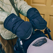 A person wearing dark navy puffer winter gloves with a white fleece lining, shown in a lifestyle setting next to a stroller.