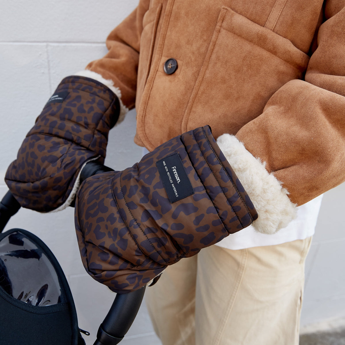 A person wearing the Finnson brown and black leopard-print quilted stroller mittens, holding a stroller handle.
