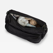 A black changing bag shown open, revealing a white blanket and a plush teddy bear inside, set against a plain background.