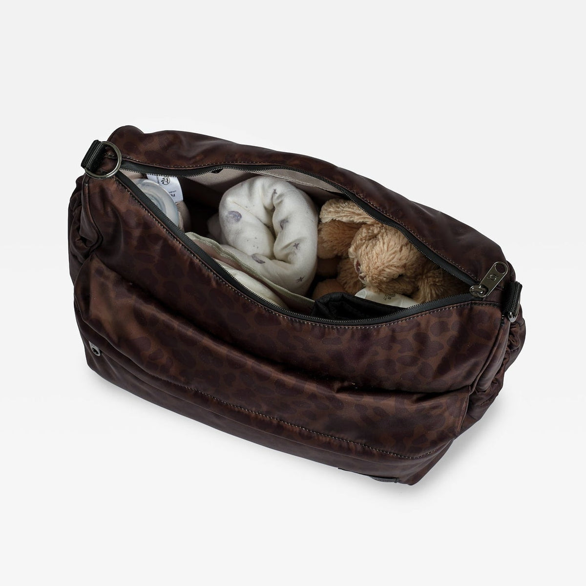 Finnson dark brown changing bag with a leopard-like pattern, shown open and filled with travel items including a blanket and a teddy bear, on a white background.