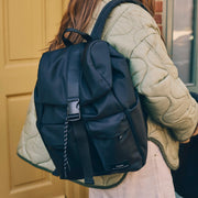 Person wearing a Finnson Black backpack with a beige quilted jacket.