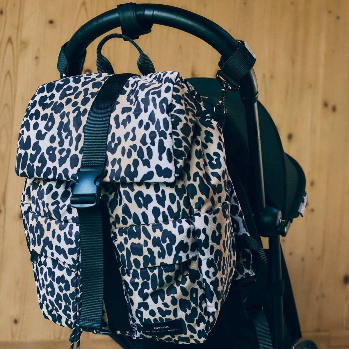Finnson Leopard print changing backpack attached to a stroller against a wooden background