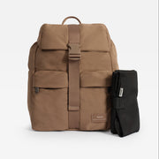 A tan Finnson Changing backpack with a central buckle strap, shown next to a black rolled travel changing mat on a light gray background. The backpack features a top flap, front zip pocket, and a small tan brand patch near the bottom right.