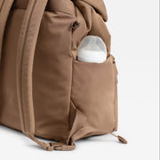 A Finnson brown changing backpack with a side pocket containing a white bottle, photographed against a white background.