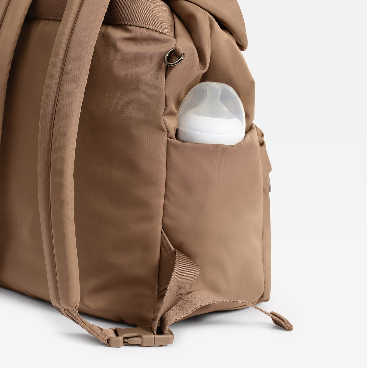 A Finnson brown changing backpack with a side pocket containing a white bottle, photographed against a white background.