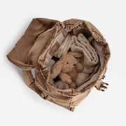 A top-down view of  the Finnson changing backpack filled with baby essentials, including a plush bunny toy, folded cream cloth, and a bottle, set against a clean white background.