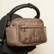 A Finnson mocha brown oversized stroller organiser bag with a front zippered pocket, shown hanging from a black stroller handle.