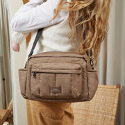 A woman carries a mocha brown Finnson crossbody oversized stroller organiser bag with a black strap in an indoor setting.