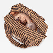 A brown and beige gingham diaper bag shown open from a top-down view, containing a plush bunny toy and baby bottles, on a light gray background.