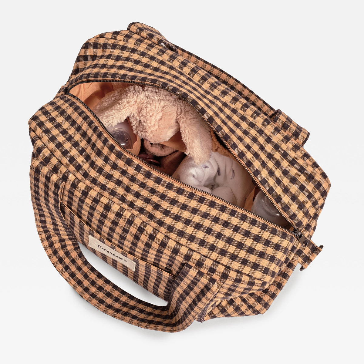 A brown and beige gingham diaper bag shown open from a top-down view, containing a plush bunny toy and baby bottles, on a light gray background.