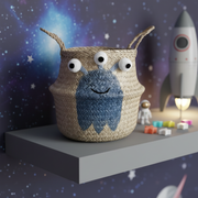 Woven basket with an alien with  googly eyes and a blue face on a shelf with space-themed decorations.