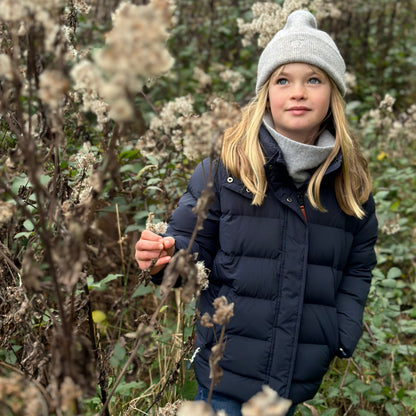 Girl wearing a light blue beanie hat and navy blue parka coat in a wild field
