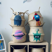 Woven baskets with colorful alien designs on a shelf against a space-themed wall.