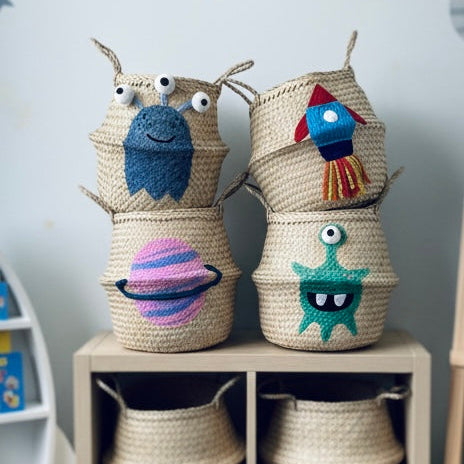 Woven baskets with colorful monster designs on a shelf against a space-themed wall.