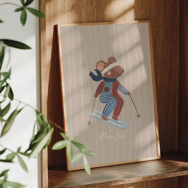 Framed illustration of a mouse skiing, it sits on a wooden shelf with plants in the background