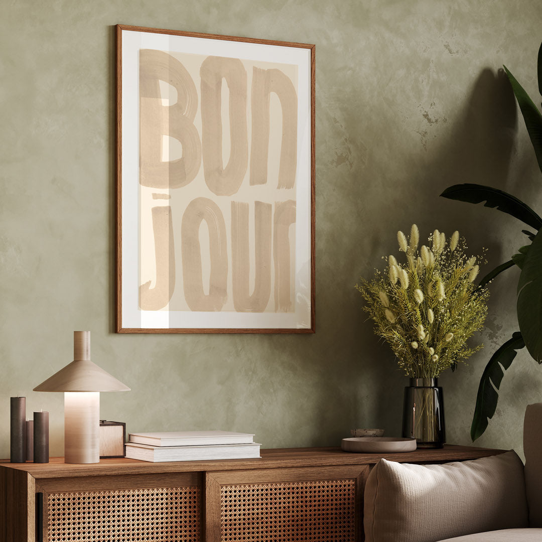 Wooden sideboard with decorative items against a green wall with a framed artwork with the word 'Bonjour'