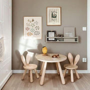 Children's room with wooden table and chairs against a gray wall with framed pictures.