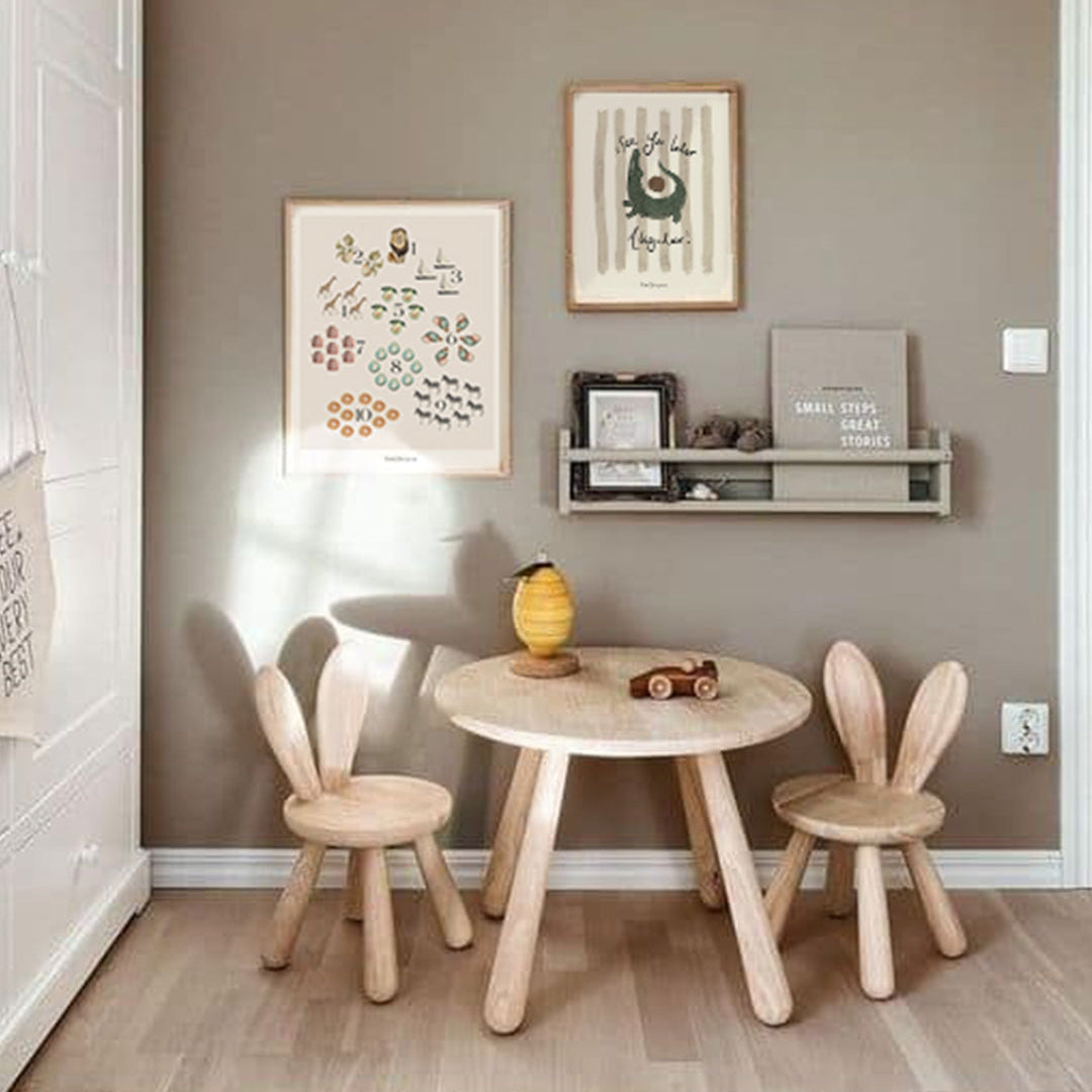 Children's room with wooden table and chairs against a gray wall with framed pictures.