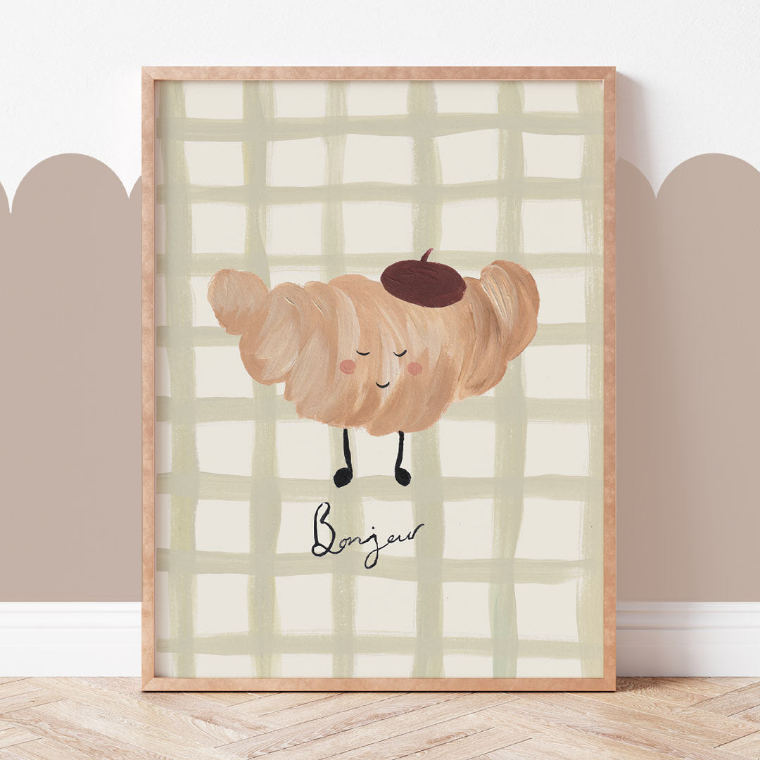 Framed artwork of a croissant character with a checkered background on a wall.