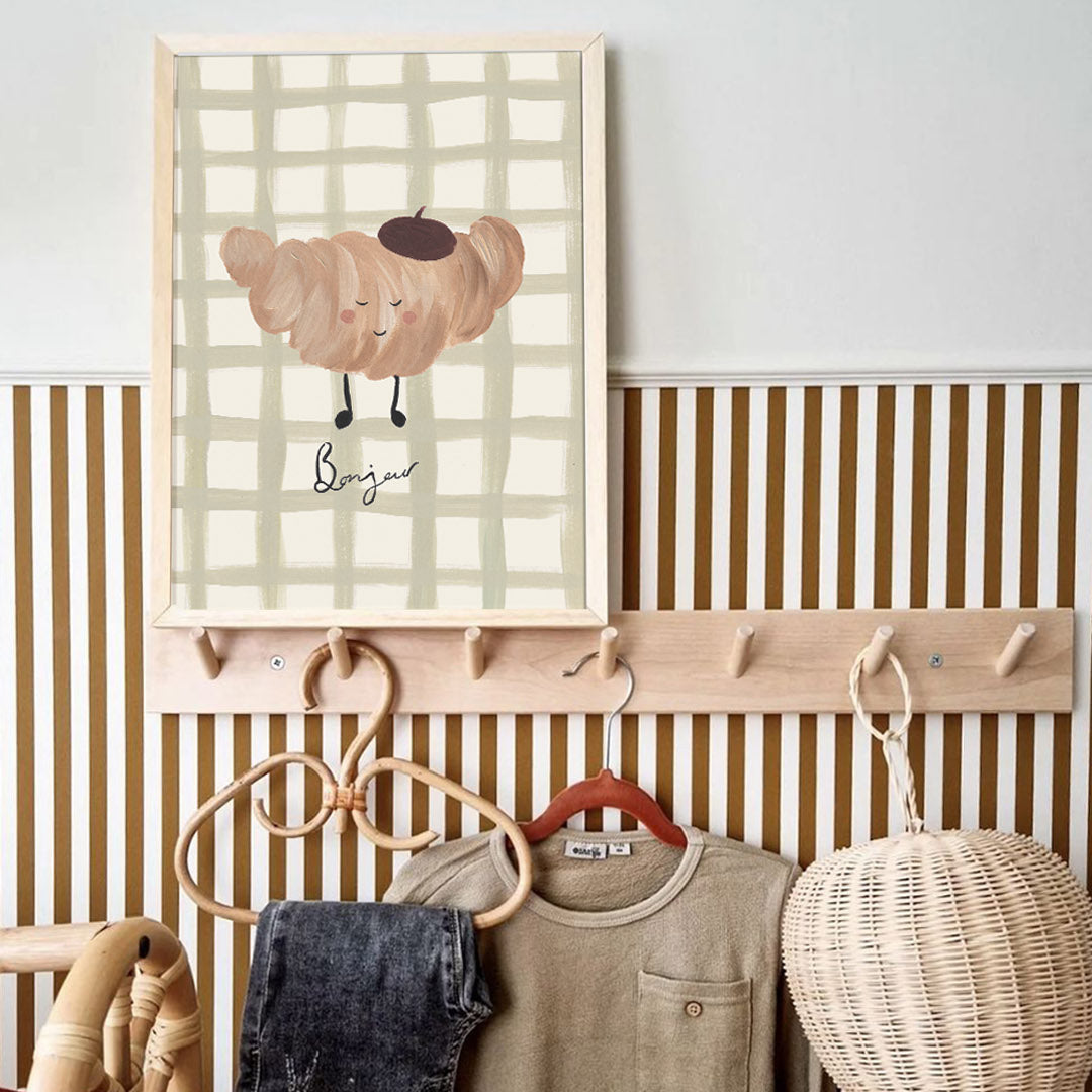 Wall-mounted coat rack with clothes and a decorative croissant art print in a room.