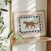 Framed artwork of a leopard on a checkered border on a wooden shelf.