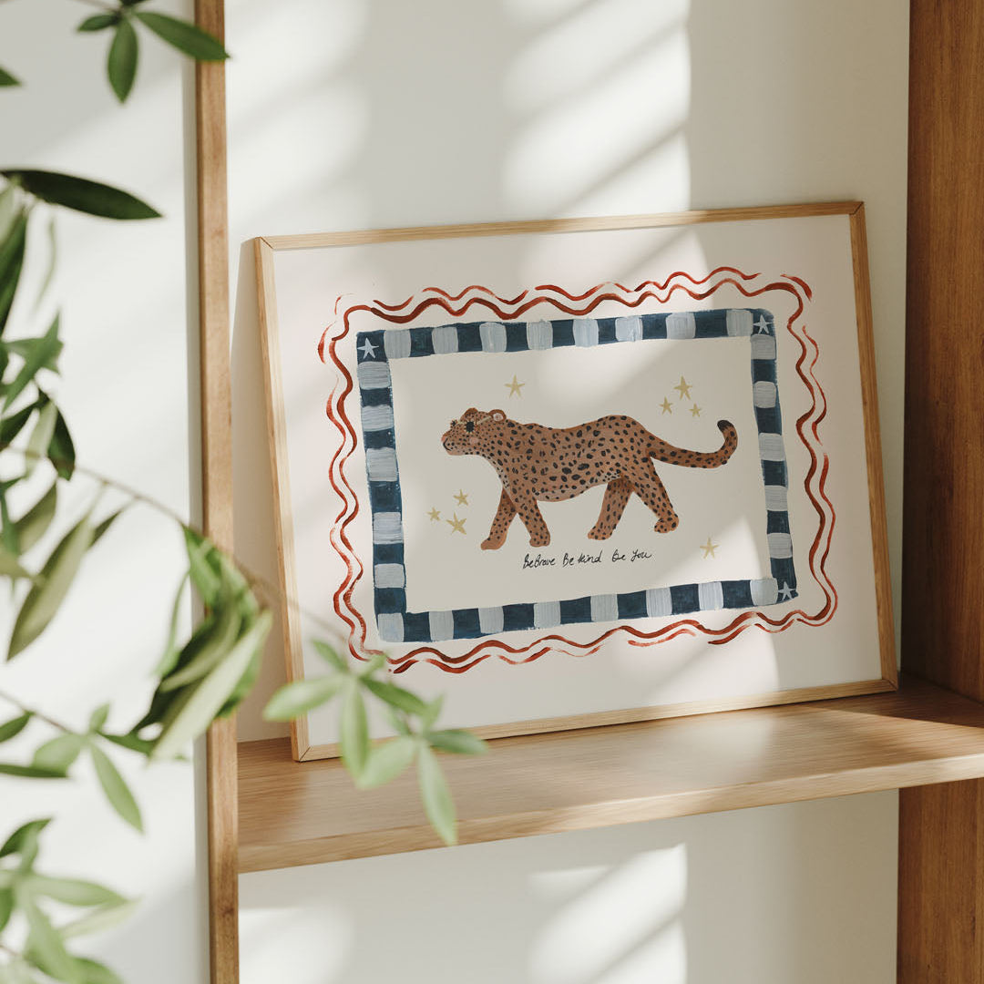 Framed artwork of a leopard on a checkered border on a wooden shelf.