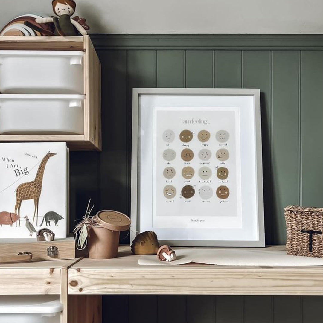 Children's play area with wooden shelf, toys, and framed artwork against a green wall.