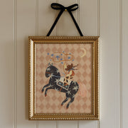 Framed artwork of a cowgirl riding a horse with a decorative pattern on a wall.