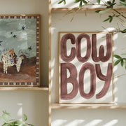 Framed artwork with 'Cow Boy' text and another illustration on a wall with plants.