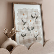 Framed floral artwork on a wall with a vase of dried flowers below.