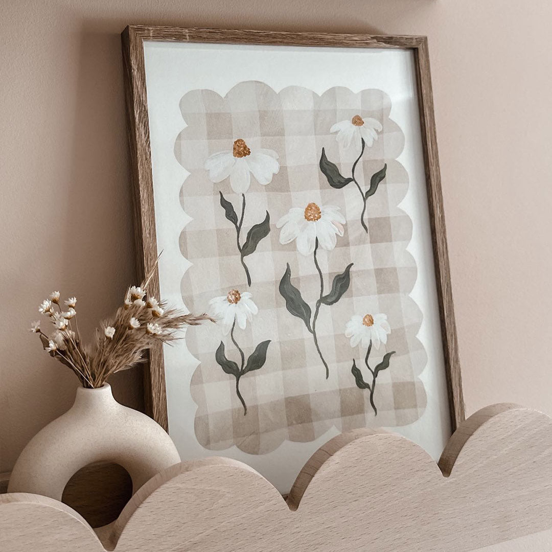 Framed floral artwork on a wall with a vase of dried flowers below.