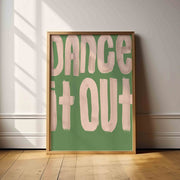 Framed poster with 'Dance It Out' text on a green background in a room with wooden floor and white walls.
