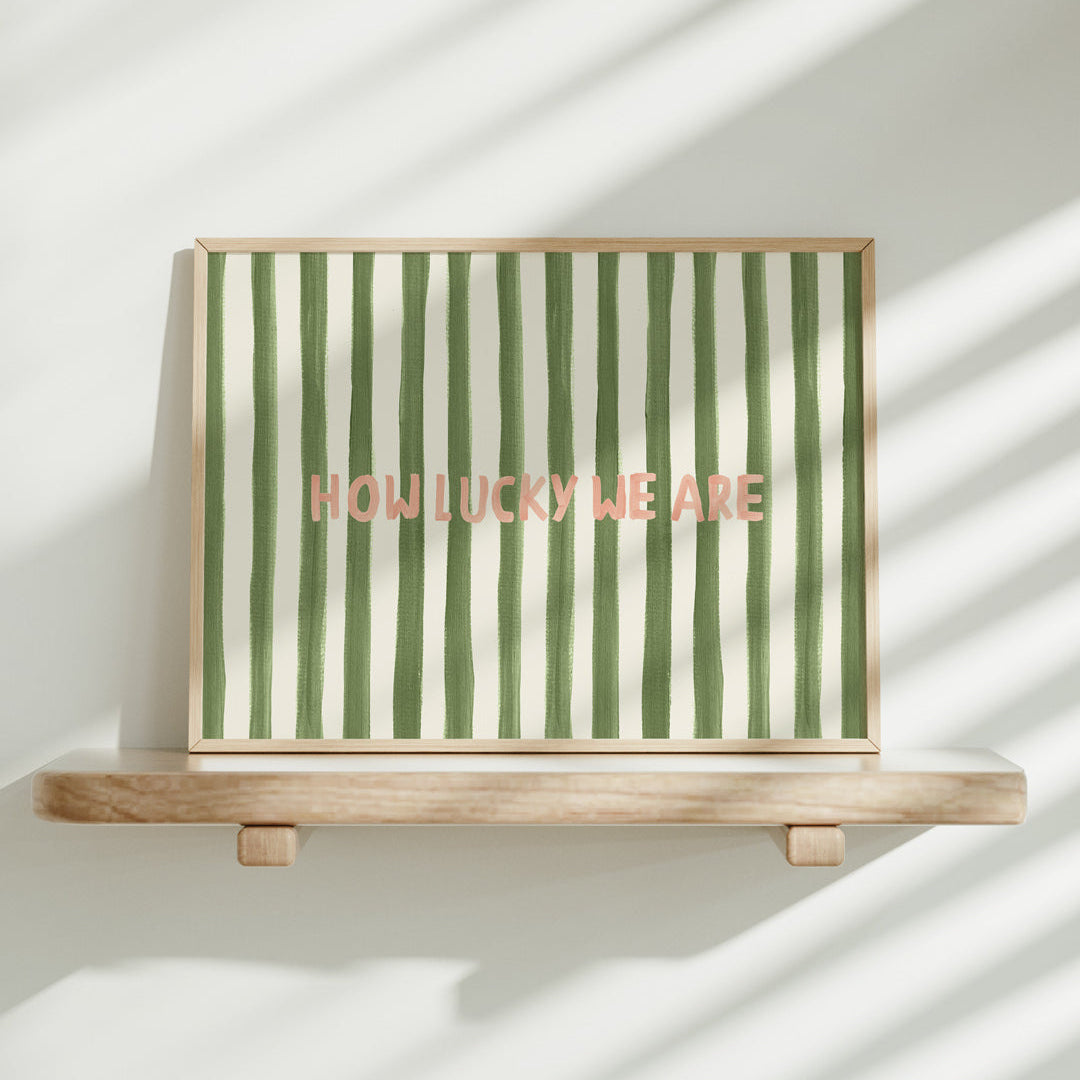 Framed artwork with green and white stripes and 'HOW LUCKY WE ARE' text on a wooden stand.