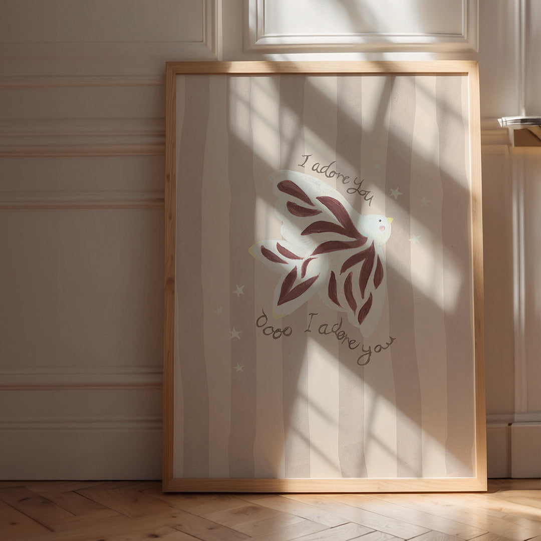 Framed artwork with a dove design and the words 'I adore you' on a wall with sunlight casting shadows.