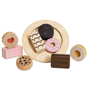 A set of wooden toy food pieces arranged on a round beige plate with floral detailing, including a pink donut, a dark chocolate cookie, a patterned rectangular piece, a heart-shaped cookie, and a brown rectangular piece labeled BOURBON, photographed on a white background.