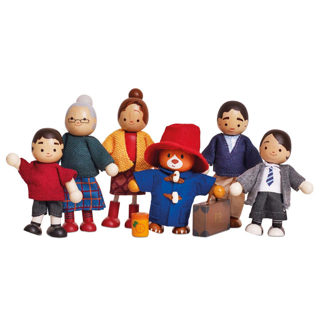 A set of wooden family and Paddington-style toy figures standing together on a plain white background. The figures include children, an older woman, a woman in a yellow coat, a bear in a red hat and blue coat holding a suitcase, and a man in a blue suit.